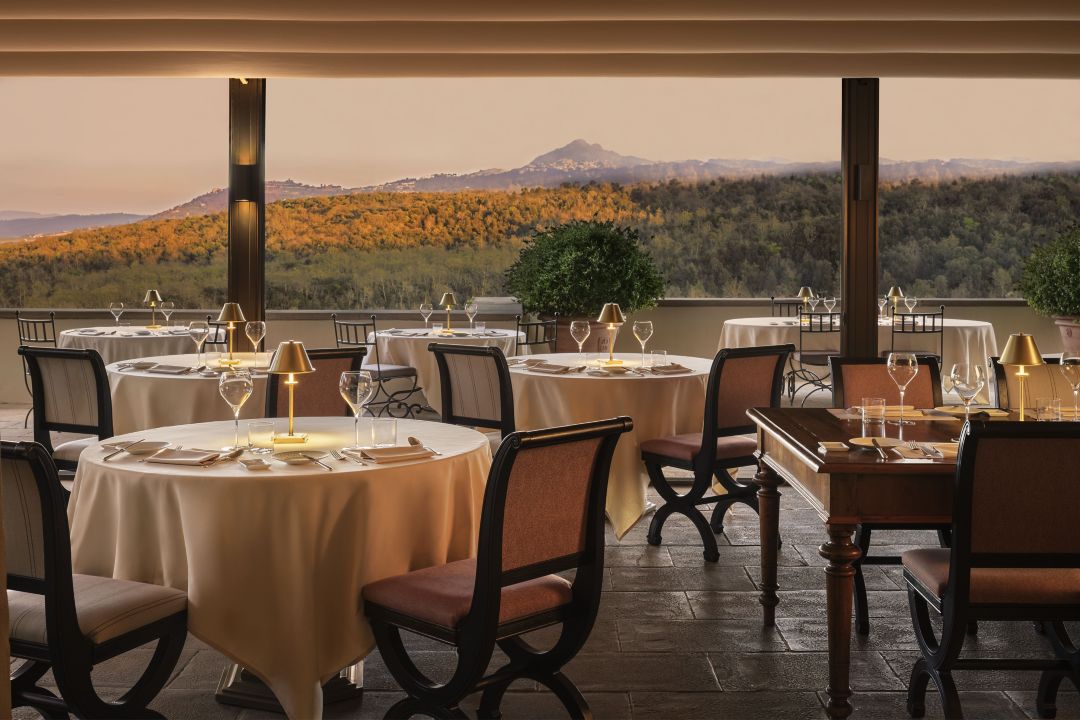 A hotel restaurant in Tuscany with tables, set against a panoramic view of rolling hills and mountains